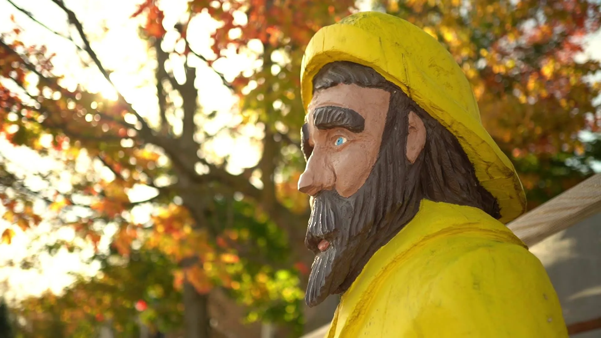 Garden gnome in yellow raincoat among autumn foliage with golden light, cottage backyard near Grand Bend